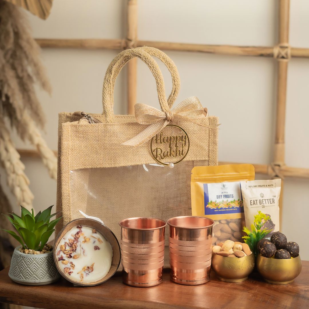 Earthy_Elegance_Pack_Hamper_Contains: Coffee Almond Laddoo (pack of 4)
, Premium Mixed Dryfruit Pack,
Coconut Shell Scented Candle,
Artificial Succulent Plant,
Copper Lining Glass (Set of 2),
Happy Rakhi Tag,
Reusable Jute Bag with Ribbon Bow