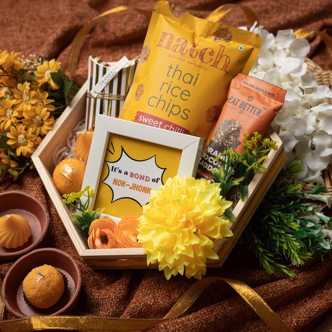 The Hamper Contains:
Premium Munching Pack,
Orange Chocolate Laddoo (pack of 4),
White Photo Frame,
Funny Quote Print (for frame),
Laddoo Shape Scented Candle,
Modak Shape Scented Candle,
Mini Golden Strips Box,
Premium Mixed Dryfruit,
Artificial Flower bunch,
Pinewood Hexagon Tray With Dual Ribbon