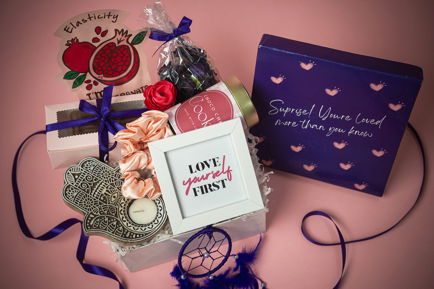 You_are_Loved_Package_Hamper that Contains: Scented Potpourri Pack, Face Mask Sheet ,Chocolate Brownies in Pink Box (2 pieces), Satin Scrunchies (pair of 2) , Choco-chip Cookie Tin Evil Eye Candle Holder, Tea Light Candle, White Photo Frame, Dream Catcher Purple, Premium Gift Box