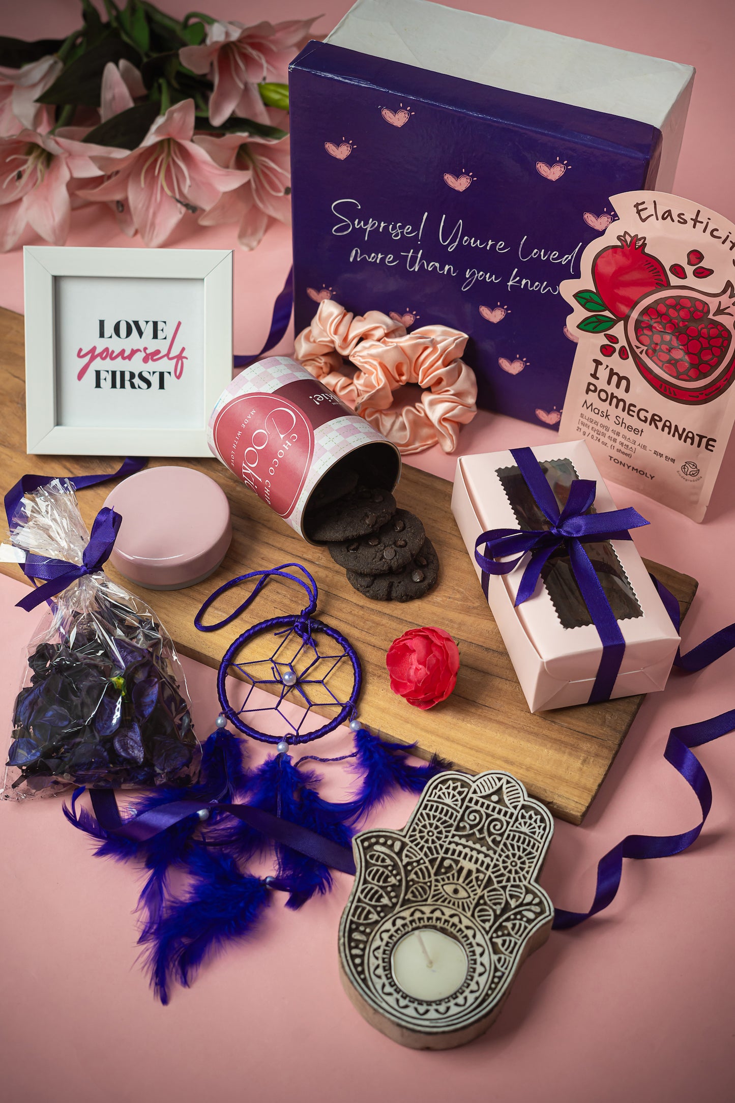 You_are_Loved_Package_Hamper that Contains: Scented Potpourri Pack, Face Mask Sheet ,Chocolate Brownies in Pink Box (2 pieces), Satin Scrunchies (pair of 2) , Choco-chip Cookie Tin Evil Eye Candle Holder, Tea Light Candle, White Photo Frame, Dream Catcher Purple, Premium Gift Box